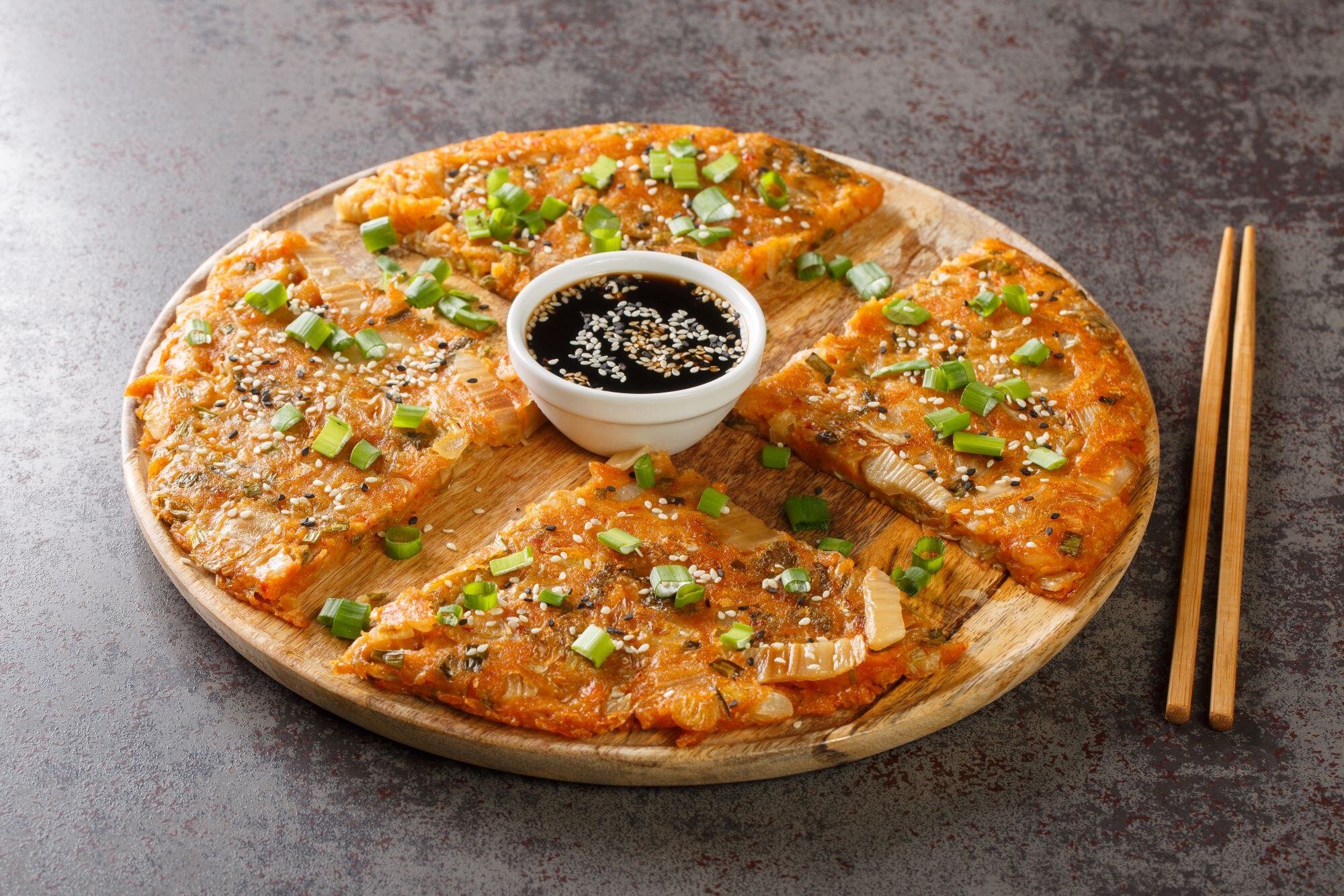 Kimchijeon is a Korean savory crispy pancake made of kimchi with flour and onion closeup on the wooden board on the table. Horizontal reduced