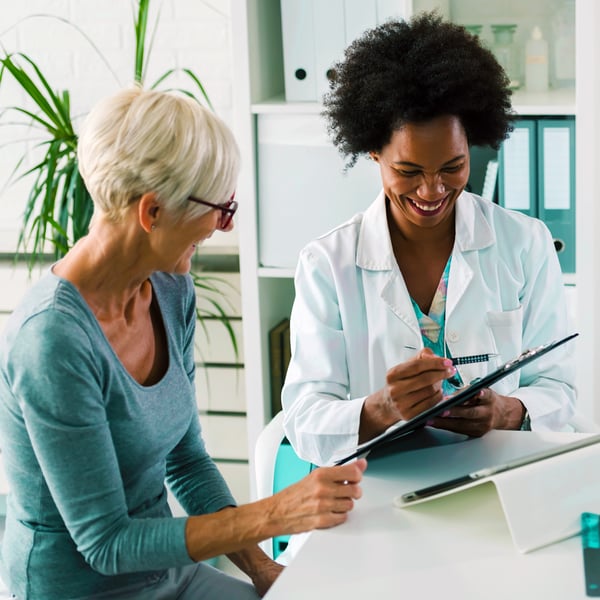 A-female-doctor-sits-at-her-desk-and-chats-to-an-elderly-female-patient-while-looking-at-her-test-results