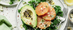 Dish with mixed greens, avocado and orange slices.