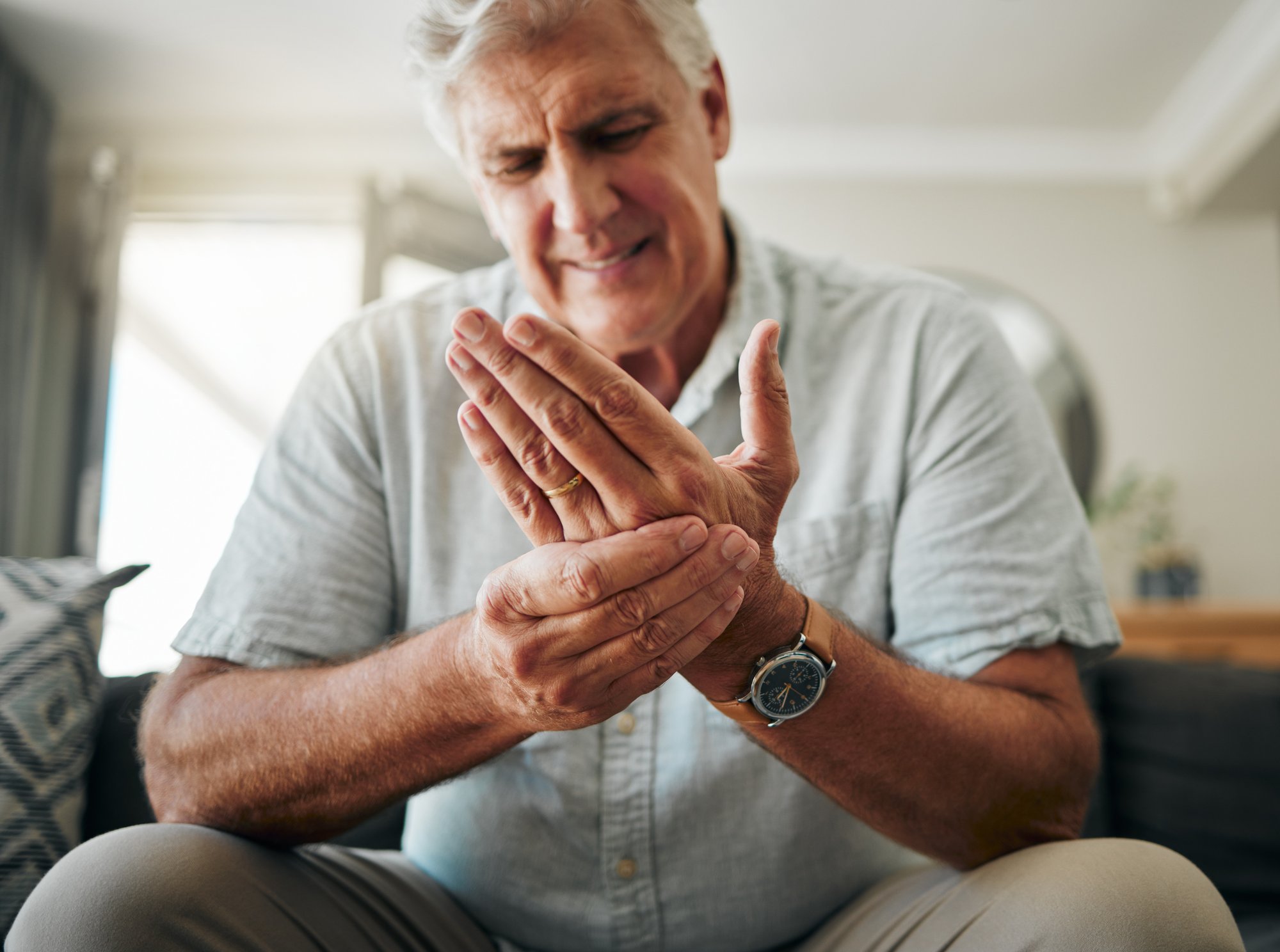 hands-pain-arthritis-with-senior-man-holding-his-hand-while-suffering-from-osteoporosis-cramp-injury-health-medical-joint-with-elderly-male-pensioner-living-room-home
