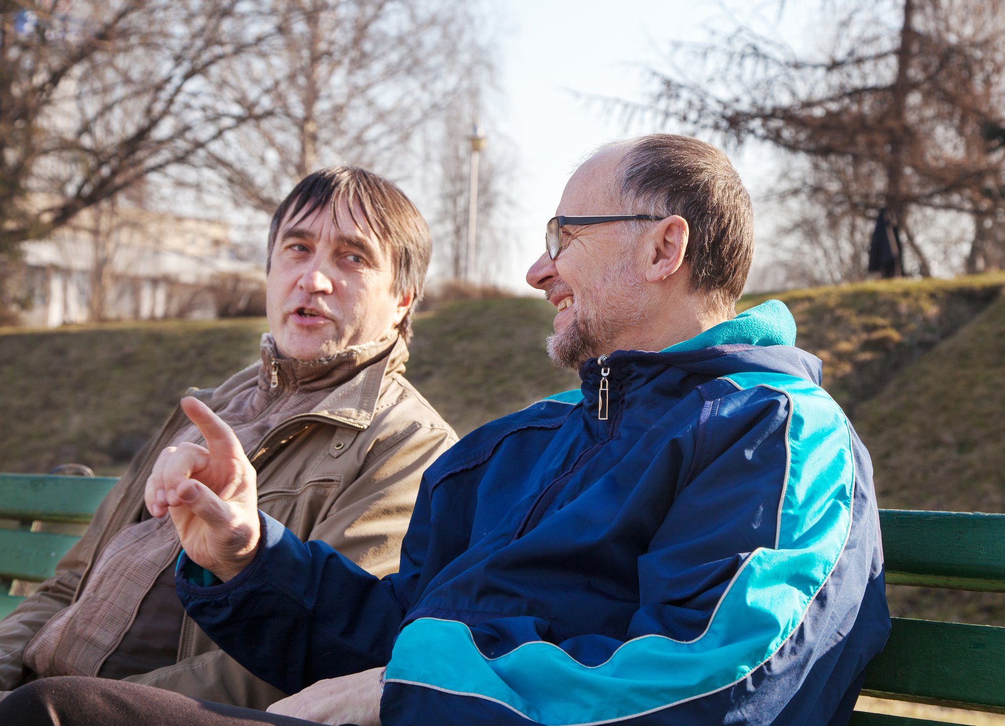 male-friends-talking-while-sitting-bench-park